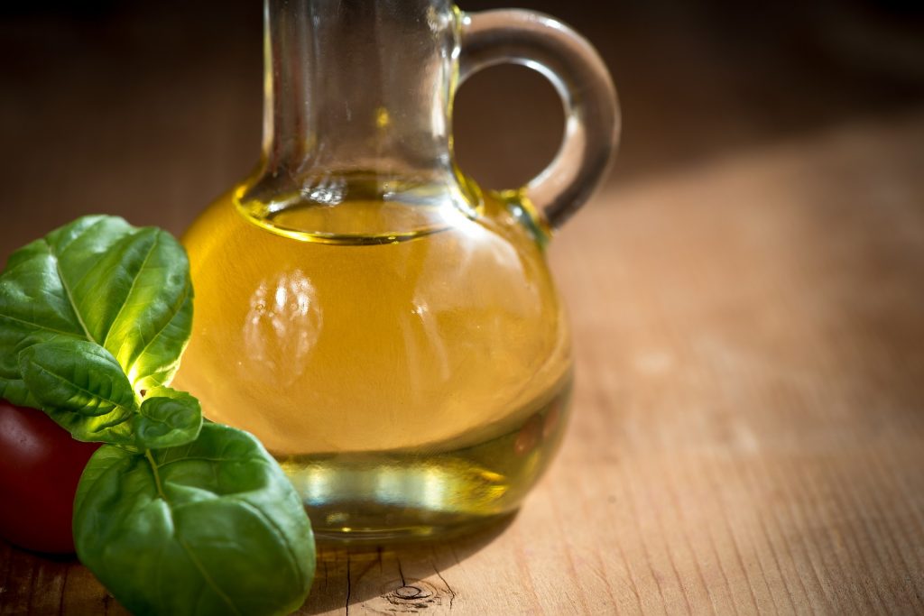 Bouteille d'huile posée sur une table à côté d'une branche de basilic